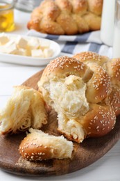 Photo of Homemade braided bread with sesame seeds on white wooden table, closeup. Traditional challah