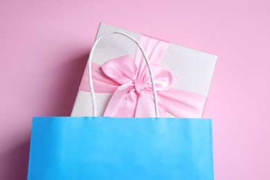 Photo of Light blue paper shopping bag with gift box on pink background, top view