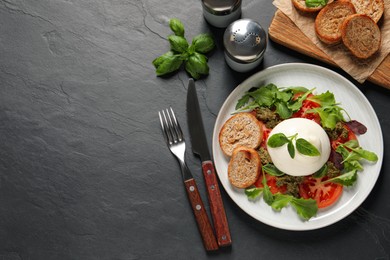 Delicious burrata salad with tomatoes, arugula and pesto sauce served on black table, flat lay. Space for text