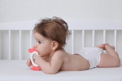 Photo of Cute little baby with teether in comfortable crib at home