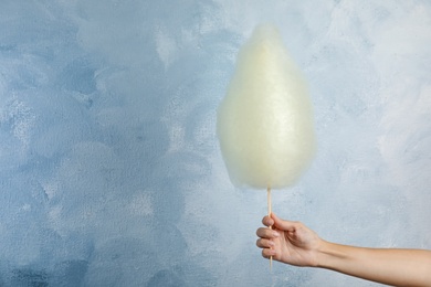 Woman holding sweet cotton candy on light blue background, closeup view. Space for text