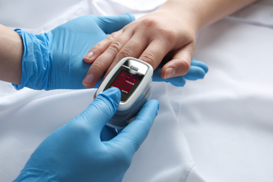 Photo of Doctor examining patient with modern fingertip pulse oximeter in bed, closeup
