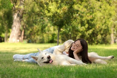 Teenage girl lying with her white Swiss Shepherd dog on green grass in park