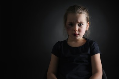 Little girl with bruises on face against dark background, space for text. Domestic violence victim