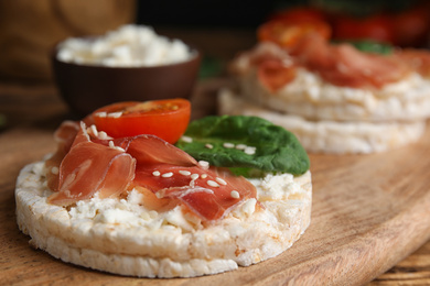 Puffed rice cake with prosciutto, tomato and basil on wooden board, closeup