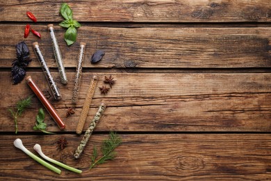 Flat lay composition with various spices, test tubes and fresh herbs on wooden background. Space for text