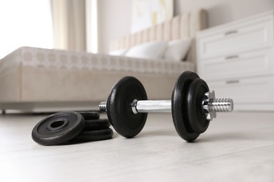 Steel dumbbell and weight plates on floor indoors. Fitness at home