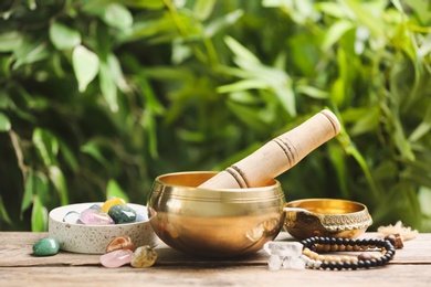 Composition with tibetan singing bowl and different gemstones on wooden table outdoors. Sound healing