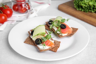 Tasty rye crispbreads with salmon, cream cheese and vegetables served on light grey table