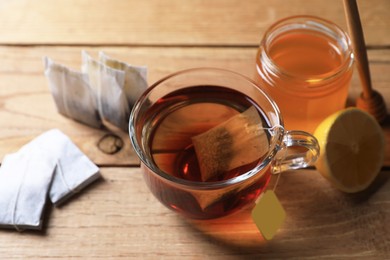 Photo of Tea bag in glass cup, honey and lemon on wooden table
