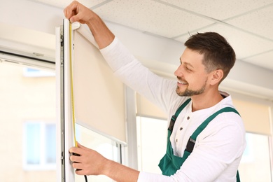 Image of Handyman with tape measure installing roller window blind indoors
