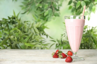 Tasty fresh milk shake with strawberries on white wooden table against blurred background, space for text
