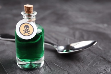 Glass bottle of poison with warning sign and spoon on grey stone table,  closeup. Space for text