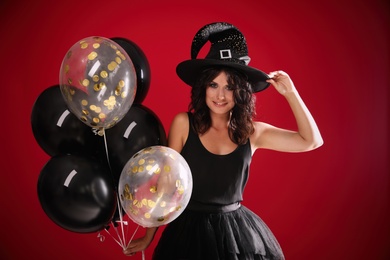 Beautiful woman in witch costume with balloons on red background. Halloween party