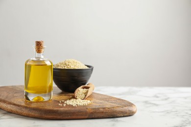 Wooden board with bottle of sesame oil and seeds on white marble table. Space for text