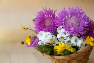 Photo of Bouquet of beautiful wildflowers in wicker basket on beige background, closeup. Space for text
