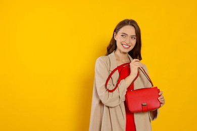 Photo of Beautiful young woman in fashionable outfit with stylish bag on yellow background, space for text