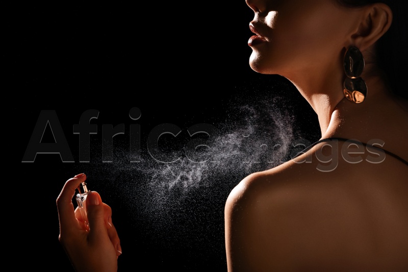 Woman spraying luxury perfume on black background, closeup