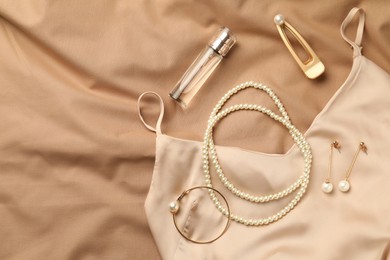 Photo of Stylish jewelry with pearls, luxury perfume and silk dress on beige fabric, flat lay