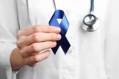 Photo of Doctor holding blue awareness ribbon, closeup view. Symbol of medical issues