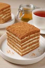 Delicious layered honey cake served with tea on wooden table, closeup