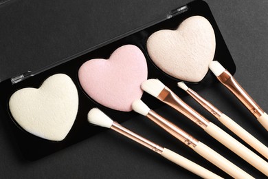 Photo of Palette of heart shaped eyeshadows with brushes on dark background, flat lay