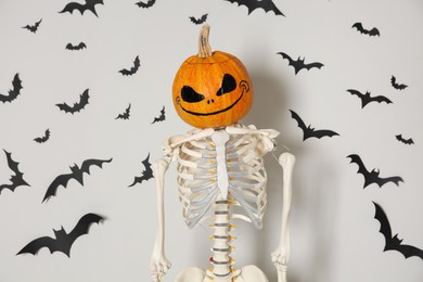 Skeleton with pumpkin head and paper bats on white wall