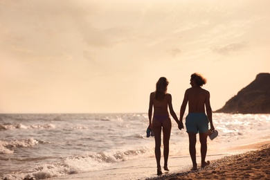 Young woman in bikini and her boyfriend walking on beach at sunset. Lovely couple
