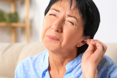 Photo of Senior woman cleaning ear with cotton swab at home, closeup