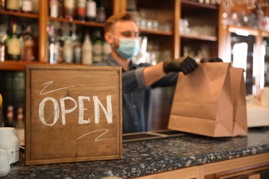 OPEN sign and blurred view of waiter with takeout orders on background. Food service during coronavirus quarantine
