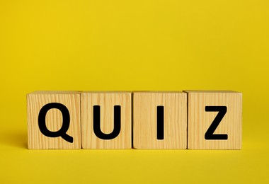 Wooden cubes with word Quiz on yellow background. Space for text