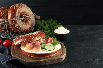 Delicious bagel with cream cheese, jamon, cucumber, tomato and parsley on black table