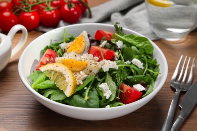 Delicious salad with boiled egg, tomatoes and cheese in bowl on wooden table, closeup