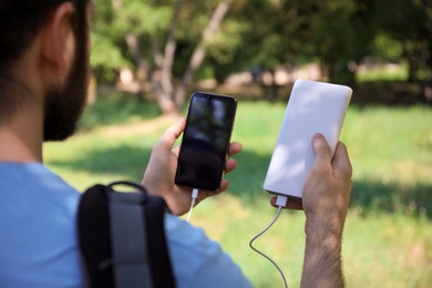 Man charging mobile phone with power bank in forest, closeup