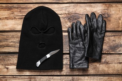 Photo of Black knitted balaclava, gloves and knife on wooden table, flat lay