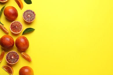 Many ripe sicilian oranges and leaves on yellow background, flat lay. Space for text