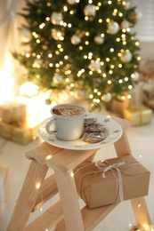 Tasty hot drink and cookies in room with Christmas tree