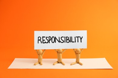 Three plasticine human figures holding card with word Responsibility on orange background