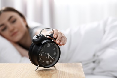 Photo of Young woman turning off alarm clock at home in morning, focus on hand. Space for text