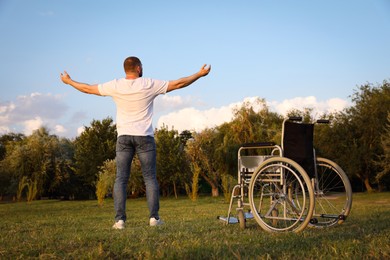 Man standing near wheelchair outdoors on sunny day, back view. Healing miracle