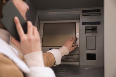 Photo of Young woman talking by mobile phone while using cash machine for money withdrawal outdoors, closeup