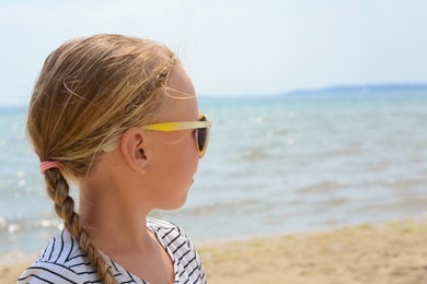 Photo of Little girl wearing sunglasses at beach on sunny day. Space for text
