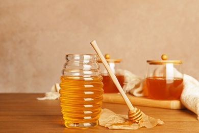 Photo of Glass jar with tasty honey and dipper on wooden table