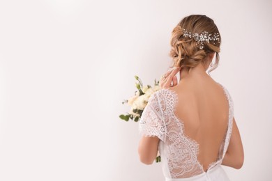 Young bride with elegant hairstyle holding wedding bouquet on white background, back view