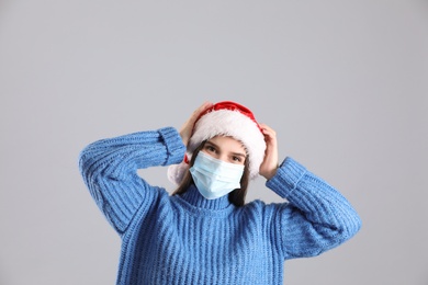 Pretty woman in Santa hat and medical mask on grey background