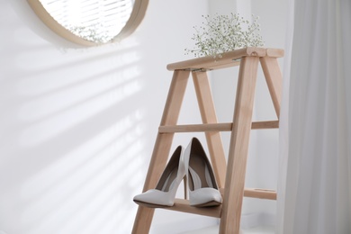 Beautiful wedding shoes on ladder and dress hanging in room, closeup