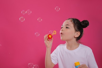 Little girl blowing soap bubbles on pink background, space for text