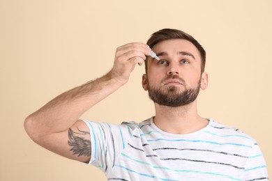 Young man using eye drops on beige background