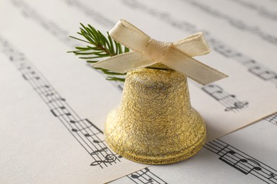 Photo of Golden shiny bell with bow on music sheet, closeup. Christmas decoration