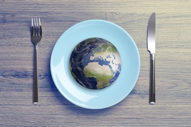 Global food crisis concept. Globe of Earth in plate and cutlery on wooden table, flat lay